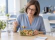 Mulher a almoçar uma salada de massa e legumes numa marmita, no espaço de refeições do escritório