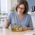 Mulher a almoçar uma salada de massa e legumes numa marmita, no espaço de refeições do escritório